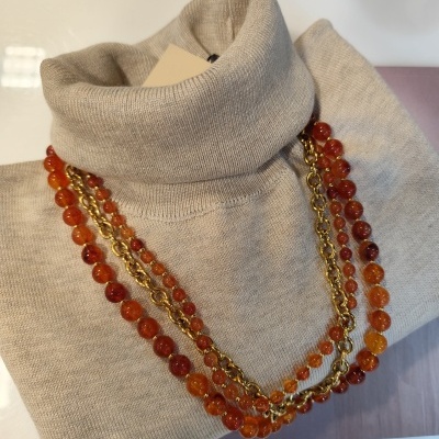 Camisola de gola alta bege com colar de contas laranja e corrente dourada