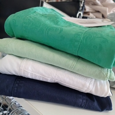 Peças de roupa empilhadas em cores verde, verde claro, branco e azul escuro com textura e padrão jacquard.