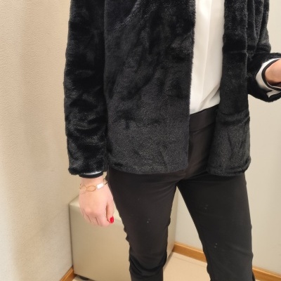 Mulher veste casaco peludo preto, camisa branca, calças pretas e sapatos pretos com detalhes dourados