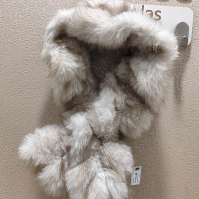 Cachecol peludo bege com pompons pendurado em cabide