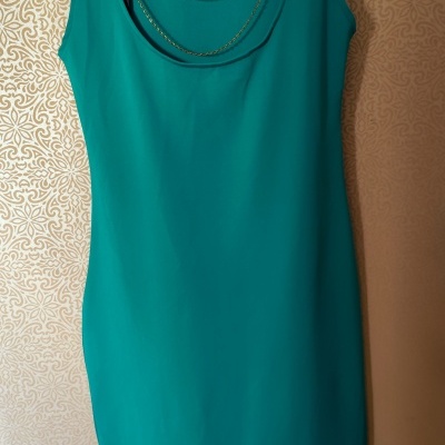 vestido verde água sem mangas pendurado em cabide preto numa parede com papel de parede decorativo dourado
