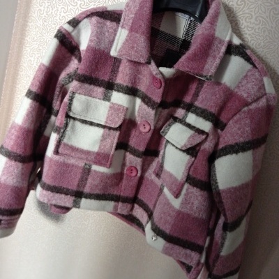 Casaco curto xadrez rosa, branco e castanho com botões e bolsos, pendurado em cabide