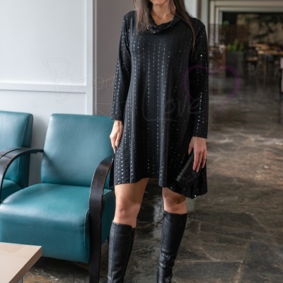 Mulher vestindo vestido preto com brilhos, botas pretas e segurando carteira preta