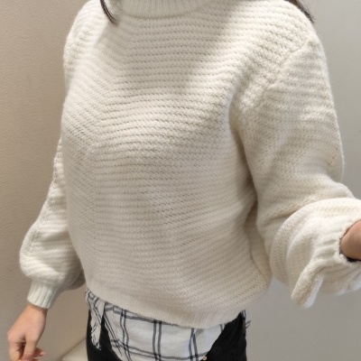 Camisola de malha branca com gola alta sobre camisa xadrez e calças pretas