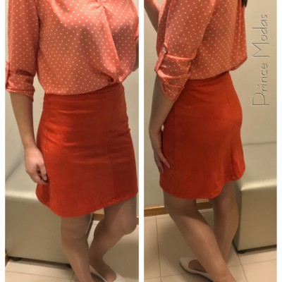 Blusa cor de salmão com bolinhas brancas e saia laranja com sapatos brancos em ambiente interno