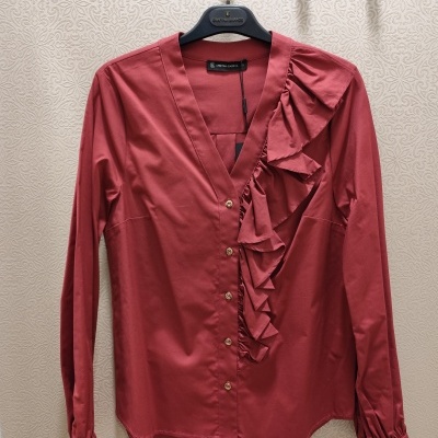 Camisa vinho com folho e botões dourados pendurada na parede