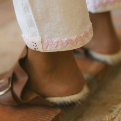 Detalhe de calças brancas com bainha rosa e sandálias castanhas com pelo