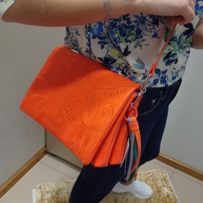 Mala de ombro laranja com padrão floral em relevo e pendente de fitas coloridas