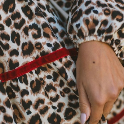 Pormenor de roupa com padrão animal print e faixa vermelha aveludada, mão ao lado.