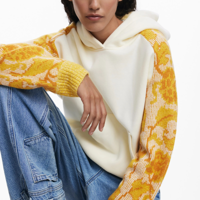 Sweatshirt com capuz creme e manga amarela com padrão floral, jeans largos azuis e ténis brancos