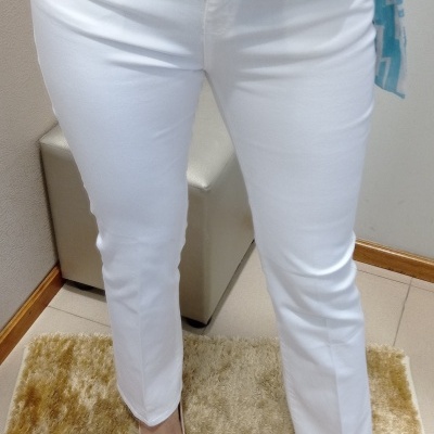 Mulher veste calças brancas justas, sapatos creme e blusa azul com padrão geométrico