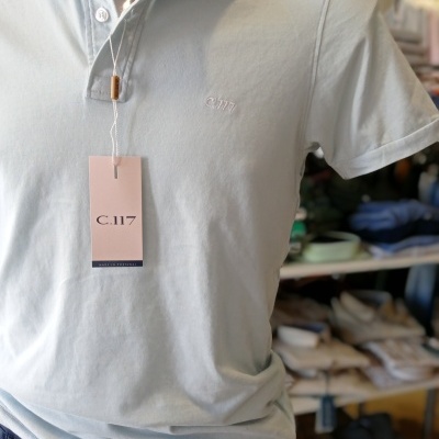 Polo azul-claro com etiqueta C.117 pendurada num manequim