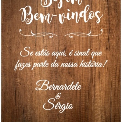 Painel de madeira com texto branco de boas-vindas e mensagem personalizada.
