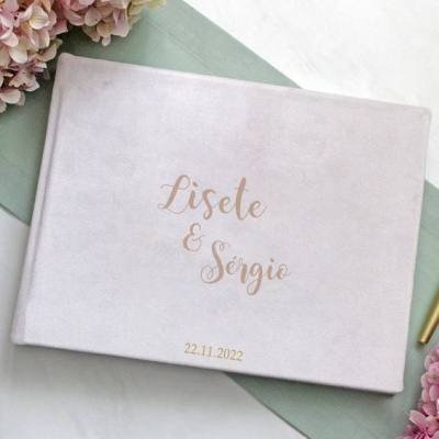 Livro de capa branca aveludada com nomes dourados no centro e data na parte inferior central