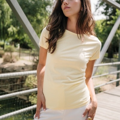 Mulher com t-shirt amarela e calças brancas numa ponte ao ar livre, logótipo TH CLOTHES no canto superior direito