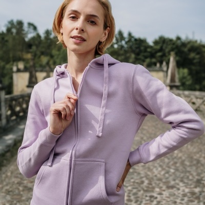 Mulher com casaco de capuz lilás e calças brancas em estrada de calçada exterior
