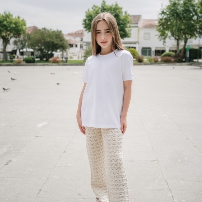 Jovem com camiseta branca e calças brancas de croché em praça exterior