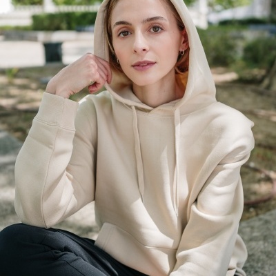 Mulher jovem com hoodie bege e calças pretas sentada ao ar livre