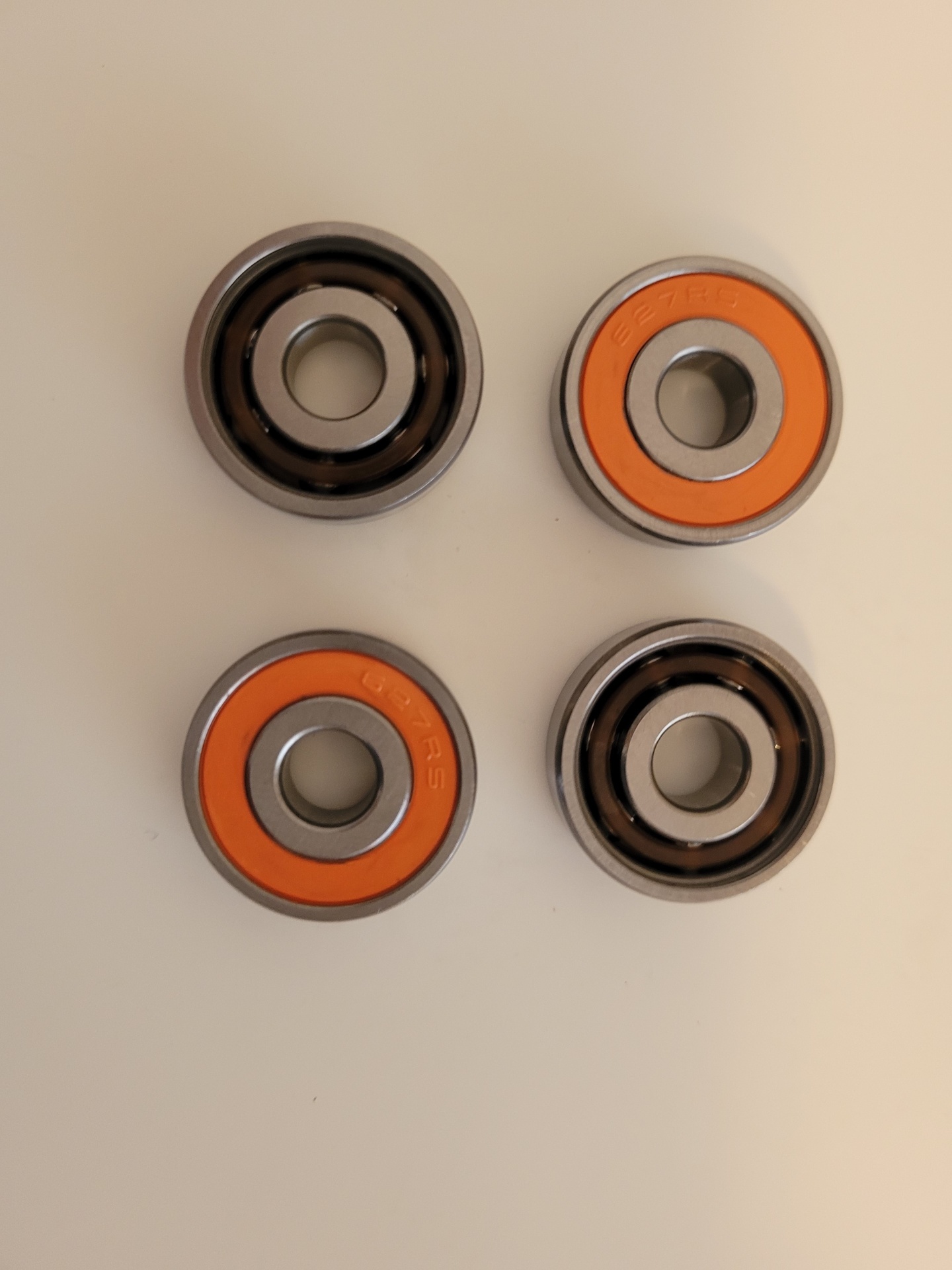 Quatro rolamentos circulares metálicos com vedação laranja e preta sobre fundo claro