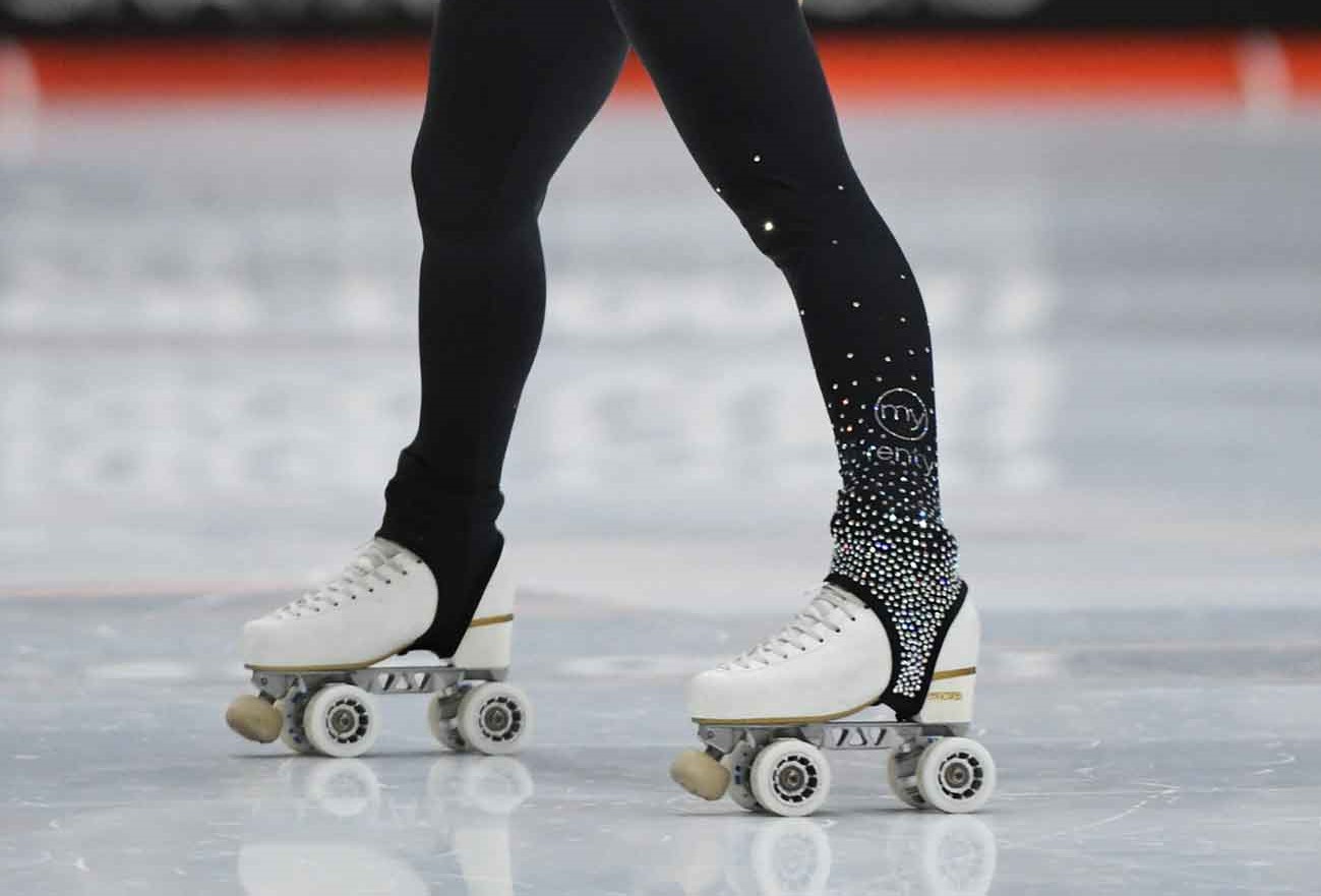 Patins brancos de rodas usados com leggings pretas decoradas em pista de patinagem