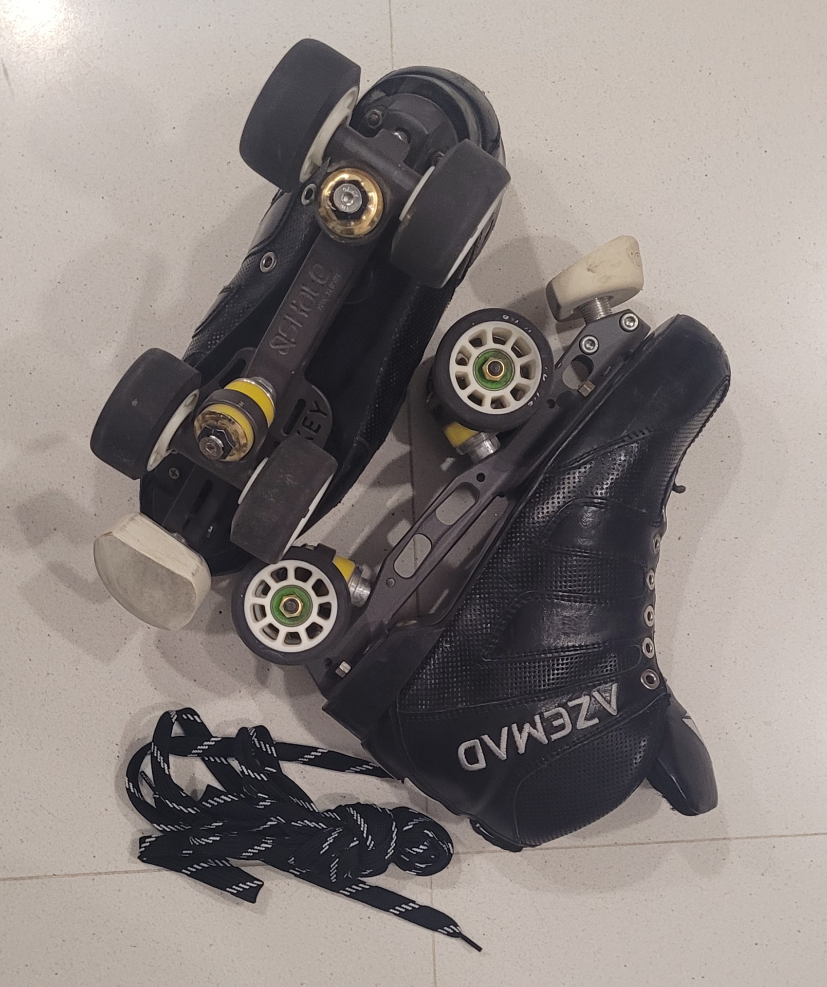 Patins de rodas pretos Azemad com rodas brancas e atacadores no chão