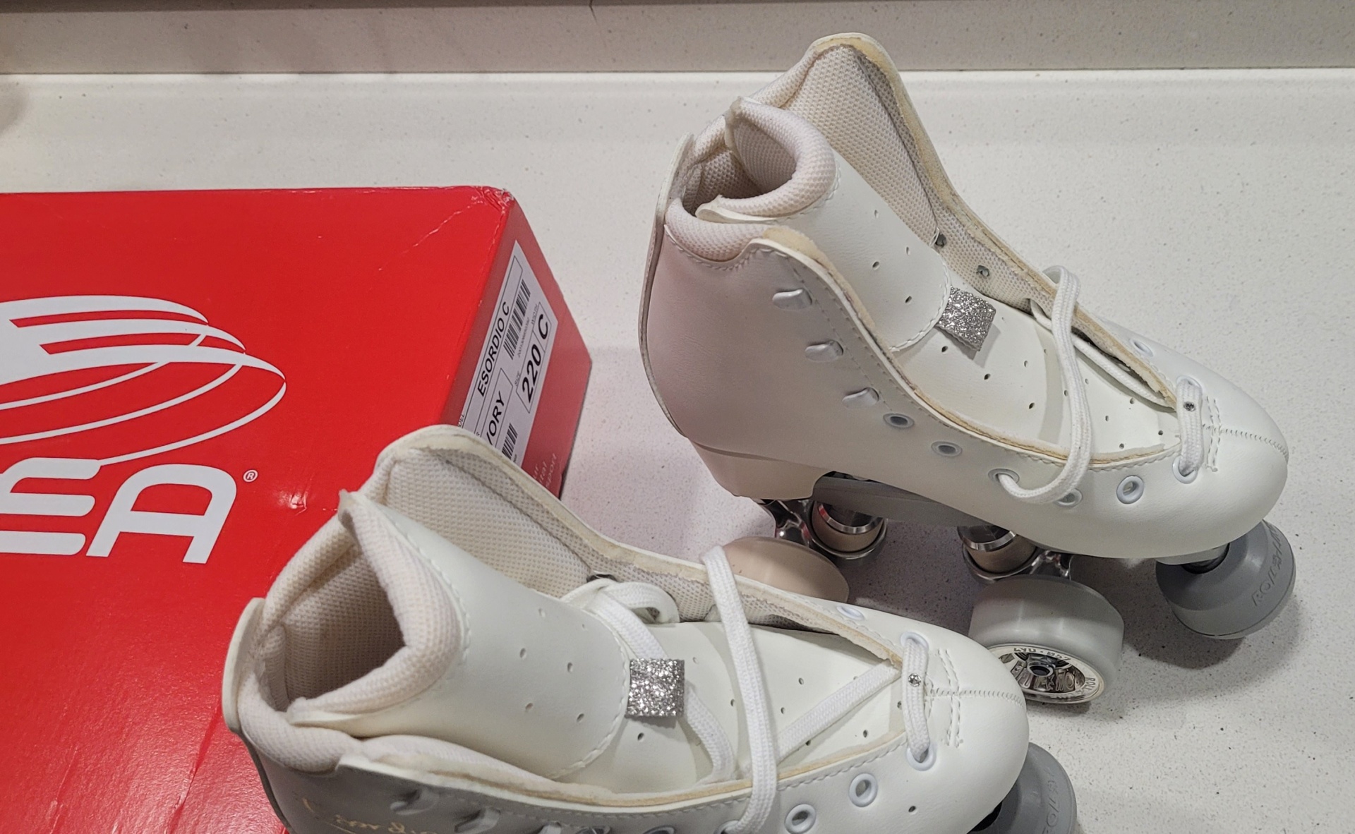 Patins em linha brancos com rodas metálicas próximos de caixa vermelha SEA