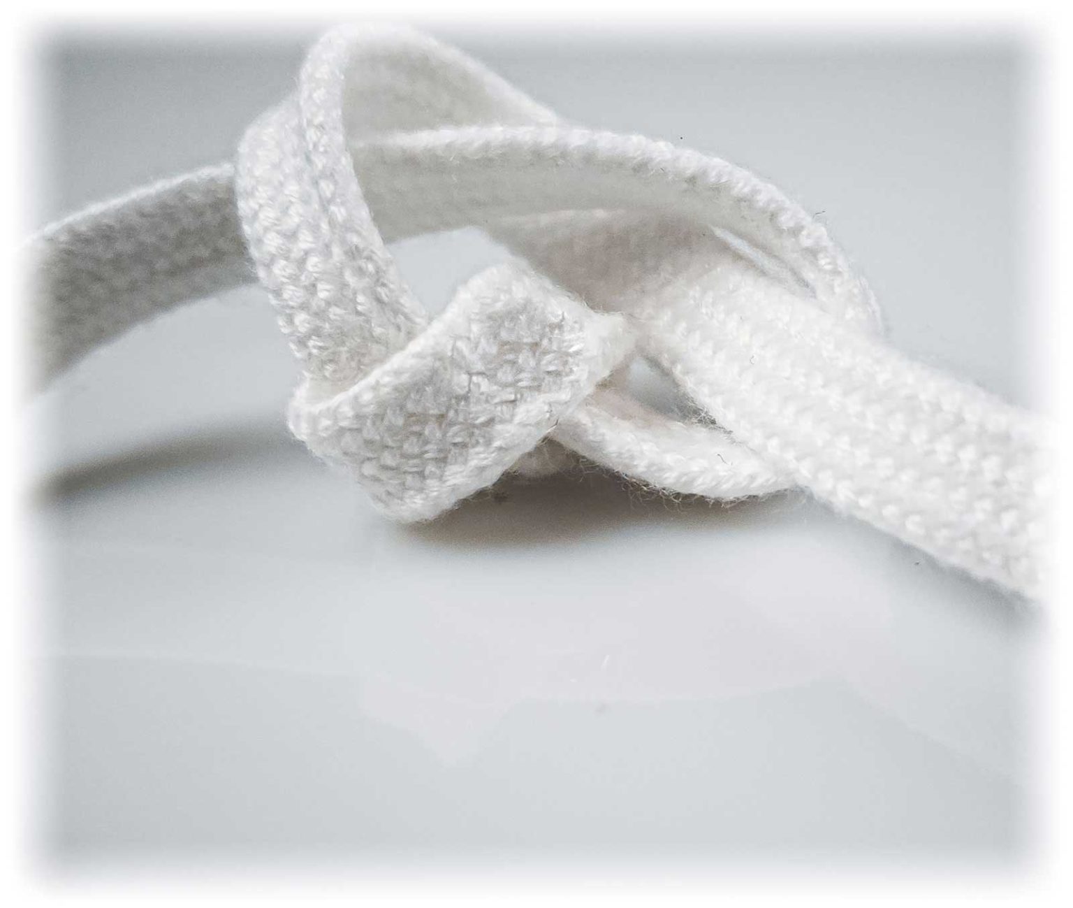 Cordão branco de tecido com nó sobre superfície branca