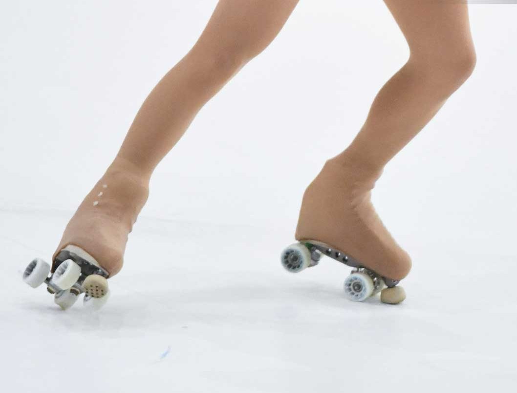 Pés com meias cor pele usando patins de quatro rodas em fundo branco