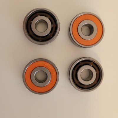 Quatro rolamentos circulares metálicos com vedação laranja e preta sobre fundo claro