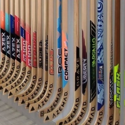 Vários tacos de hóquei em madeira com várias marcas e cores alinhados num suporte branco