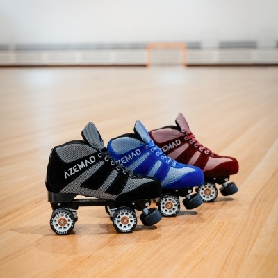Três patins de quatro rodas nas cores preta, azul e vermelha, com texto AZEMAD, em chão de madeira