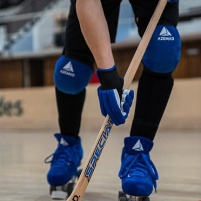 Jogador de hóquei em patins com equipamento azul e preto segurando stick de madeira e disco preto com logo AZEMAD