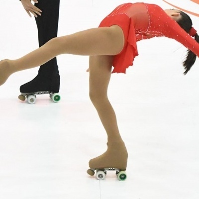 Patinadora com vestido vermelho e patins a deslizar sobre uma superfície branca.