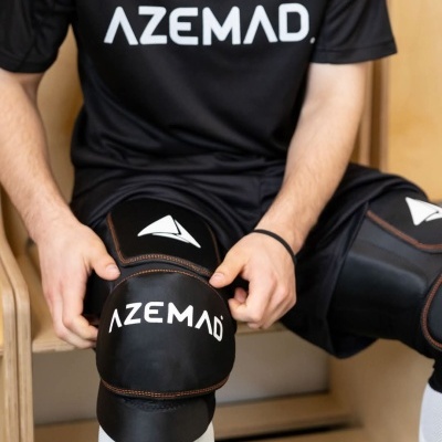 Pessoa a colocar proteções de joelho negras AZEMAD com t-shirt preta AZEMAD