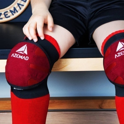 Proteção desportiva vermelha e preta AZEMAD em joelhos de criança com meias vermelhas e calções pretos sentado