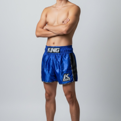 Homem com calções de boxe azuis e sem camisa, fundo cinza claro.