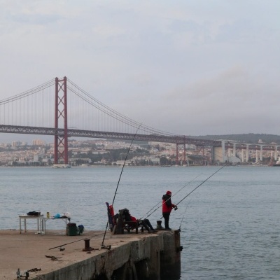 pessoas a pescar num cais junto a uma ponte vermelha sobre um rio