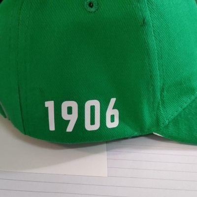 Boné verde com número 1906 branco, fotografado sobre papel