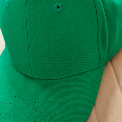 Boné verde liso com ilhós sobre superfície bege