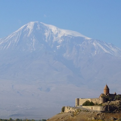 Castelo antigo com igreja sob uma grande montanha nevada e céu azul.
