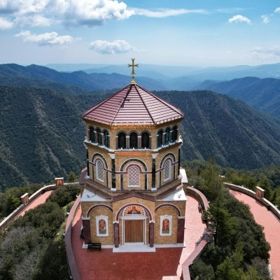 Edifício religioso octogonal numa montanha com cúpula vermelha e cruz