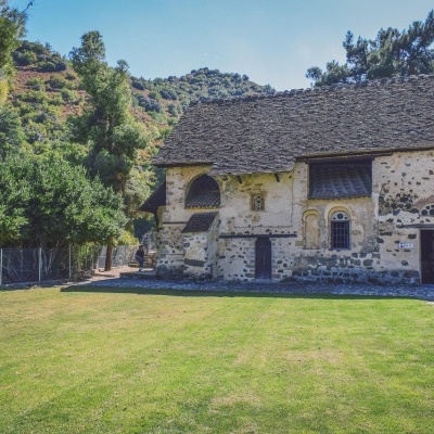 Edifício antigo de pedra com telhado de ardósia e uma cruz branca num campo verde