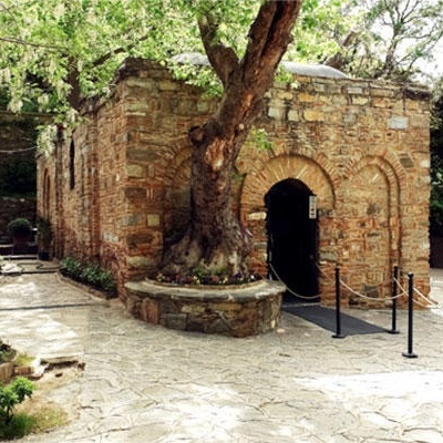 Pequeno edifício de pedra com porta arqueada e caminho de pedra em área arborizada