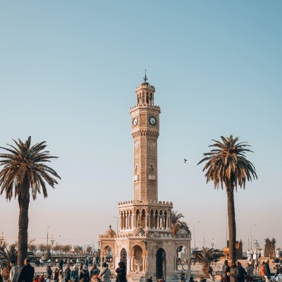 Torre do relógio histórica numa praça com palmeiras e pessoas a passear