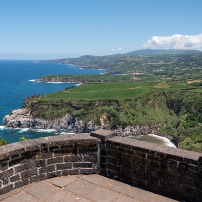 Mureta de pedra com vista para a costa, mar e colinas verdes ao fundo