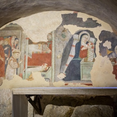 Frescos antigos numa parede curva de gruta com figuras humanas, incluindo mulher e criança.