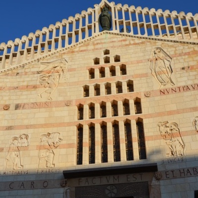 Fachada de igreja com janelas verticais, esculturas em pedra e inscrições em latim