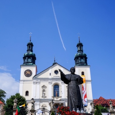 igreja branca com duas torres e estátua religiosa em frente com flores