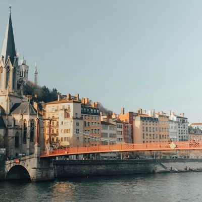 Igreja antiga de pedra junto a um rio com ponte vermelha e edifícios coloridos ao fundo