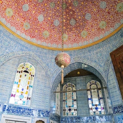 Interior com azulejos azuis, vitrais coloridos, teto em cúpula vermelho decorado e candeeiro pendente